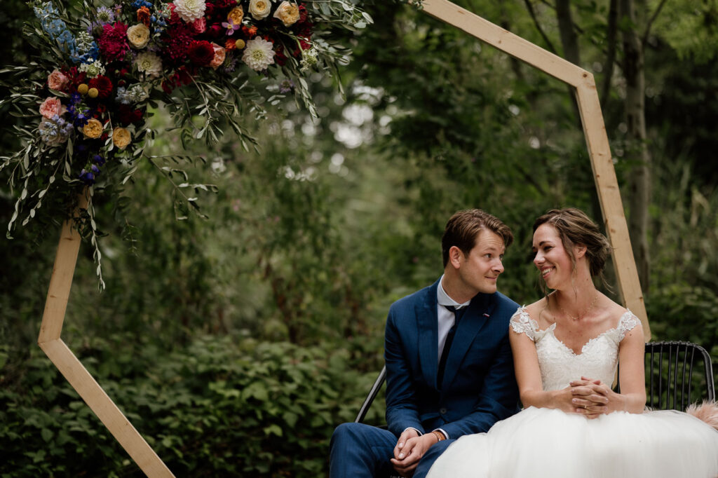 bruidspaar kijkt verliefd naar elkaar. op de achtergrond een mooi bloemstuk